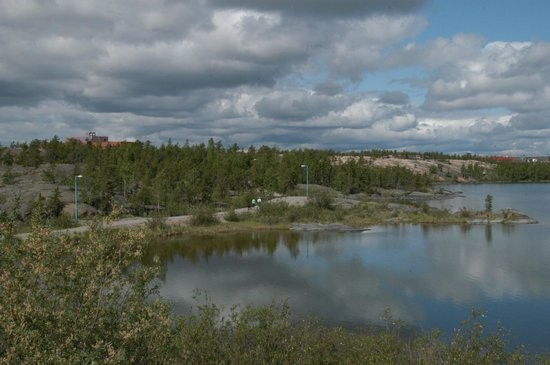 Glassy lake reflecting low clouds on a sunny day, with evergreen trees surrounding it