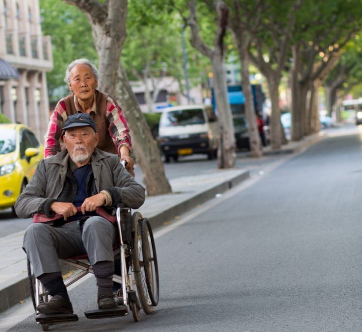 Woman Pushing Old Man In Wheelchair, Street Of Shanghai