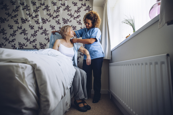 Home Caregiver helping a senior woman get dressed in her bedroom.