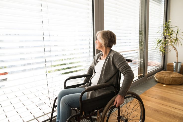 senior woman in wheelchair at home in her living room, looking out the window.