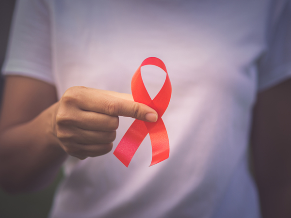 Red color ribbon awareness on young woman hand background: World aids day symbolic concept .