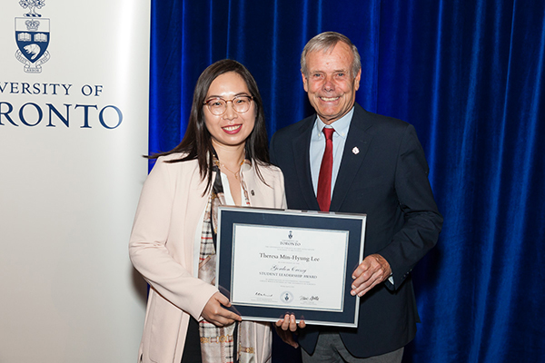 Blue back drop with Theresa Lee and Gordon Cressy in foreground holding plaque.University of Toronto, Convocation Hall, April 22, 2019.