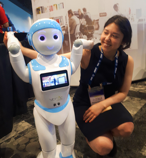 Maria Nunez kneeling at level of humanoid robot that is white and blue