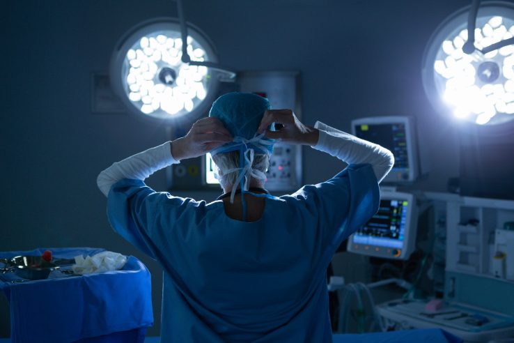 Rear view of female surgeon putting her surgical mask in operating room.