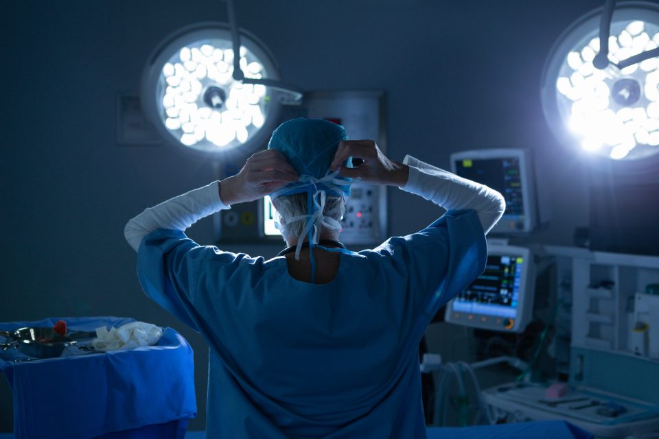 Rear view of female surgeon putting her surgical mask in operating room.