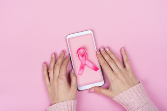 Hands holding mobile phone with pink cancer ribbon.
