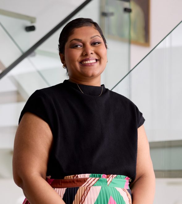 A brown woman with short hair, wearing a black top and a colourful skirt