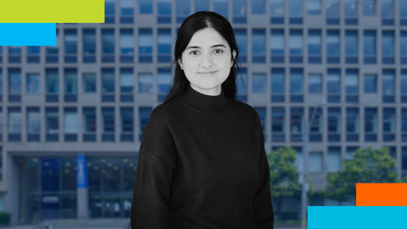 Professional portrait of a woman with long dark hair wearing a black turtleneck, standing in front of a blue-toned urban building. The background includes modern architecture and hints of greenery. The image features colorful geometric accents in green, blue, and orange on the edges.