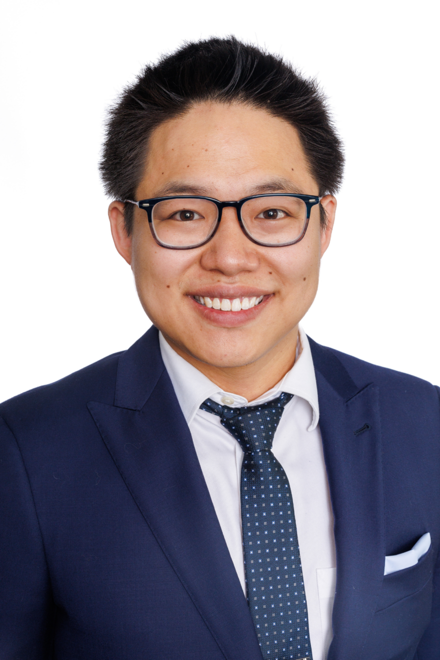 A person, a 2025–26 Vector Scholar, wearing a dark blue suit jacket, white dress shirt, and a dark blue tie with small white squares, in front of a plain white background.