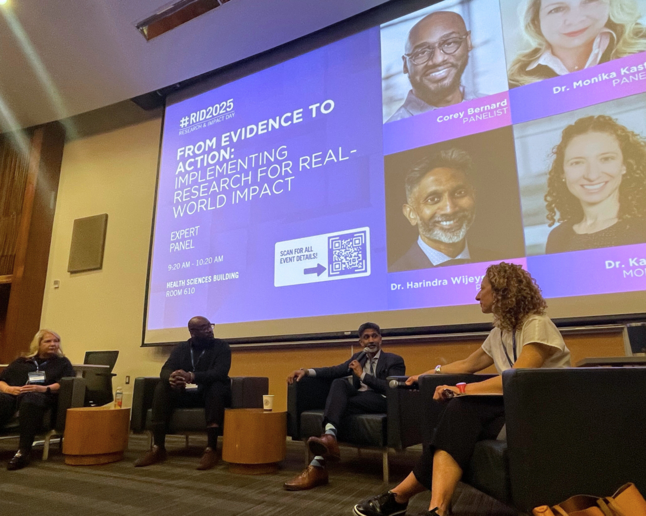 The 21st Annual Research and Impact Day expert panel discussion with a screen displaying the session title "From Evidence to Action: Implementing Research for Real-World Impact.